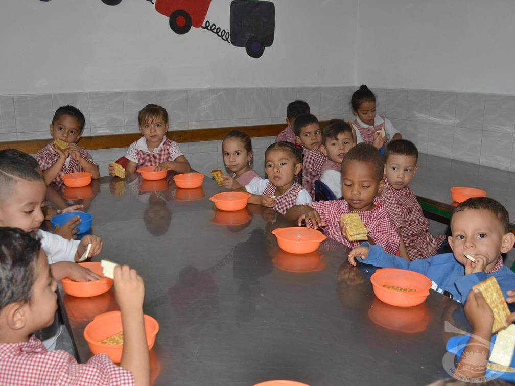 Niños reunidos en mesa alimentándose.