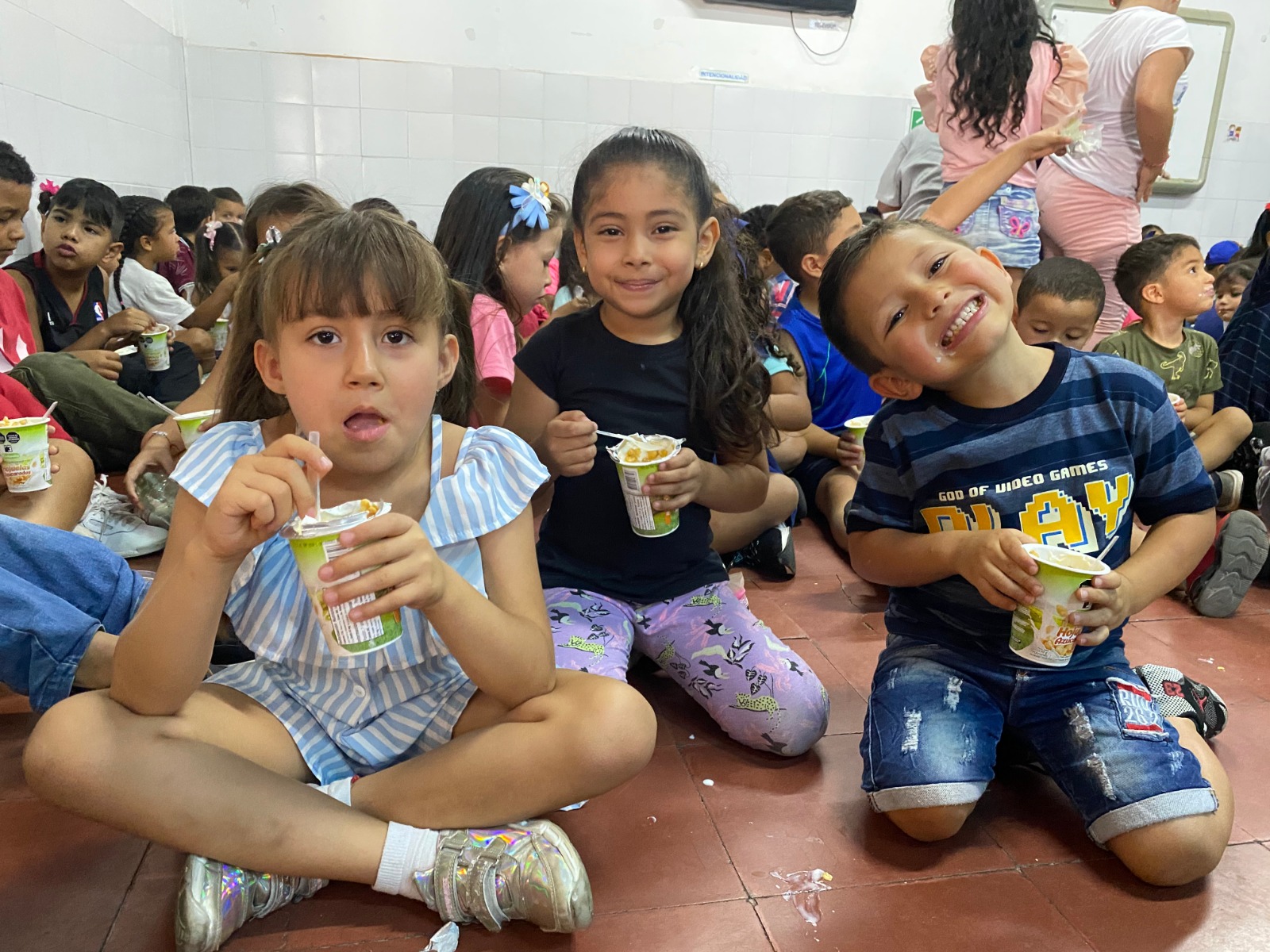Tres niños alimentandose y sonrientes, sosteniendo alimentos.